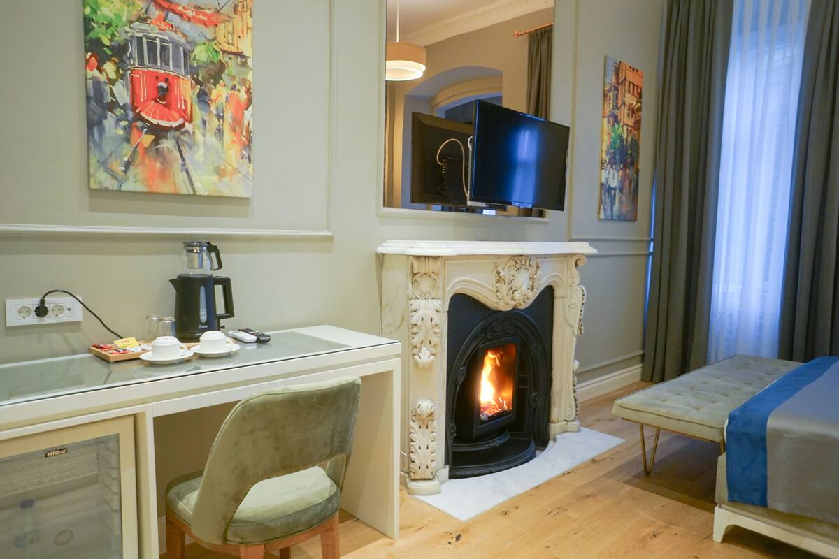 A hotel room with a fireplace, a television mounted above it, a dining area with a coffee maker, and a bed with a blue blanket.
