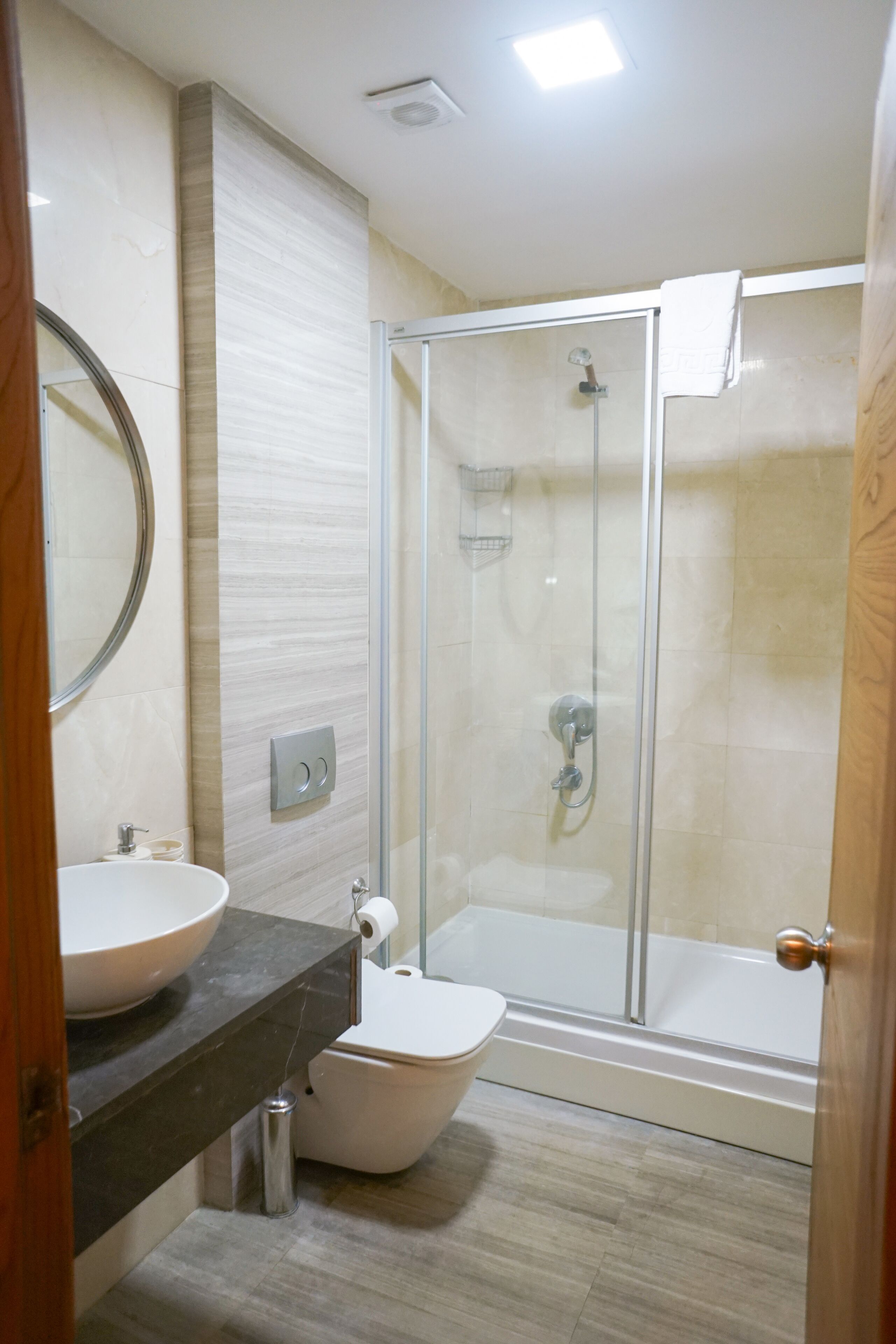 A modern bathroom with a glass-enclosed shower, a round mirror, a white sink, and a toilet.