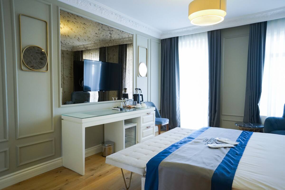 A hotel room with a large bed, a desk with a mirror, a television, and a window with curtains.