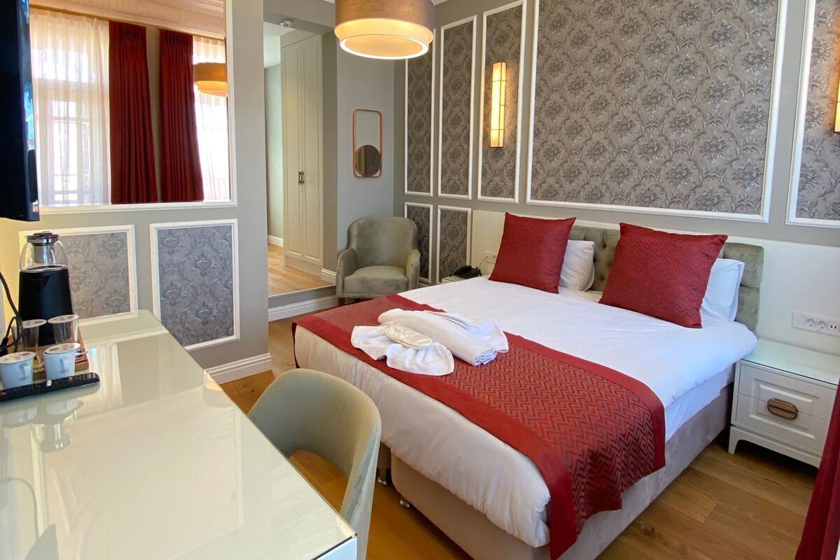 A hotel room with a large bed, a desk with a computer, a chair, and a mirror.