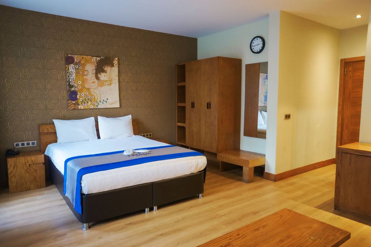 A bedroom with a bed, wooden wardrobe, bedside table, and a clock on the wall.
