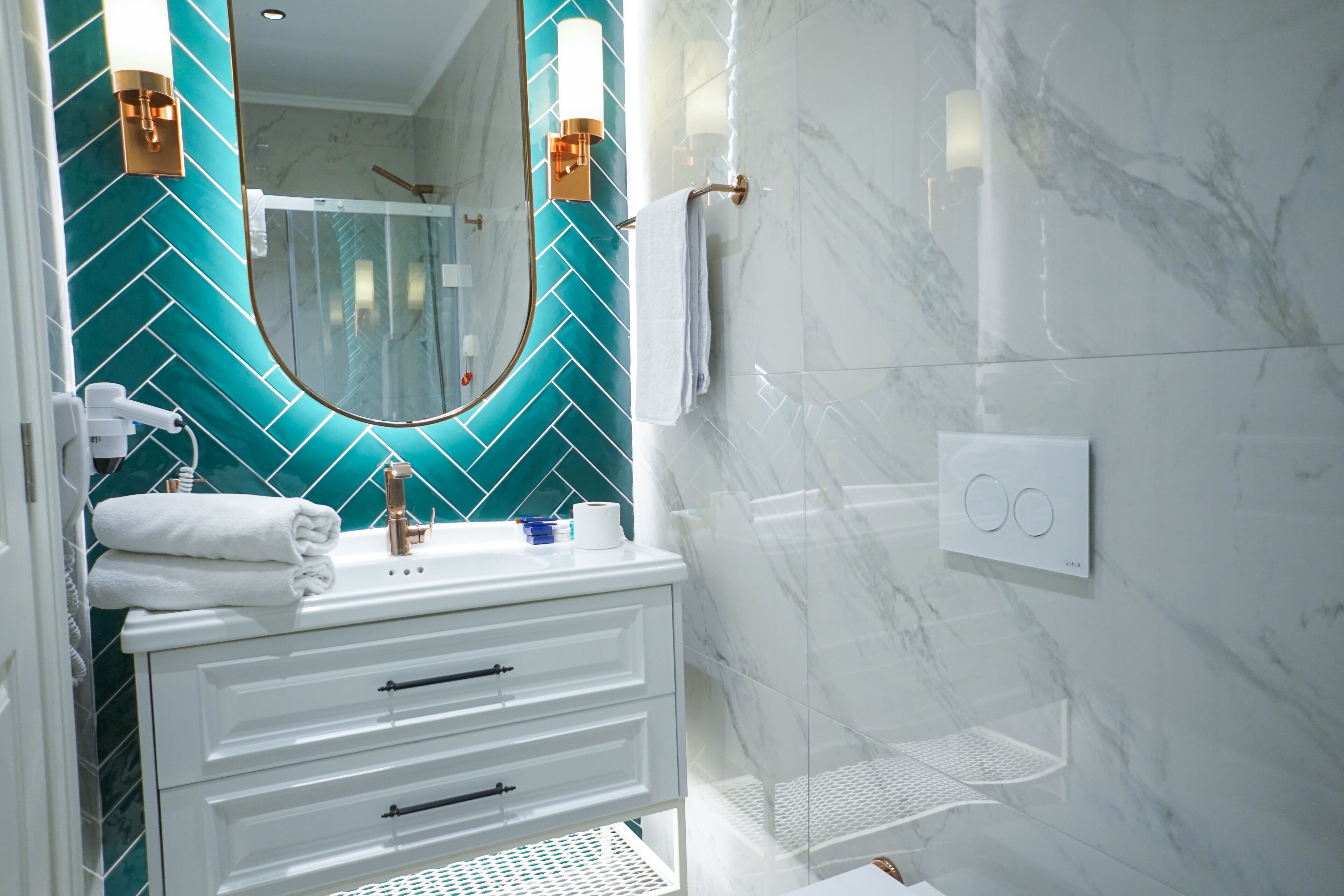 Un baño moderno con un tocador blanco, un espejo con revestimiento verde azulado y una zona de ducha.