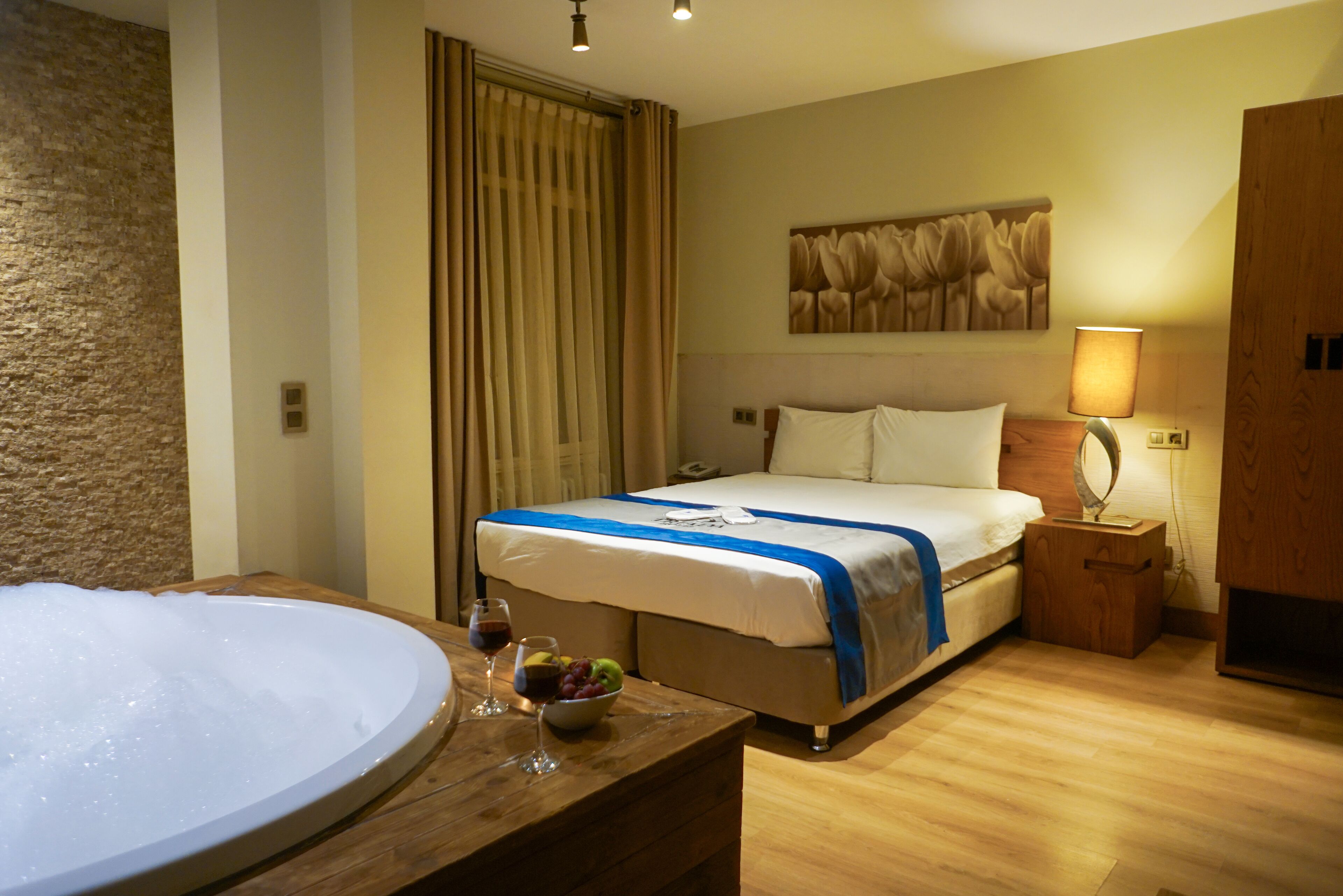 Habitación de hotel con una bañera grande, una cama con una manta azul, un frutero y una lámpara en una mesita de noche.