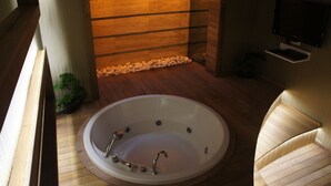A modern bathroom with a large oval bathtub, wooden flooring, a small plant, and a television mounted on the wall. - Triada Hotel Taksim (Istanbul)