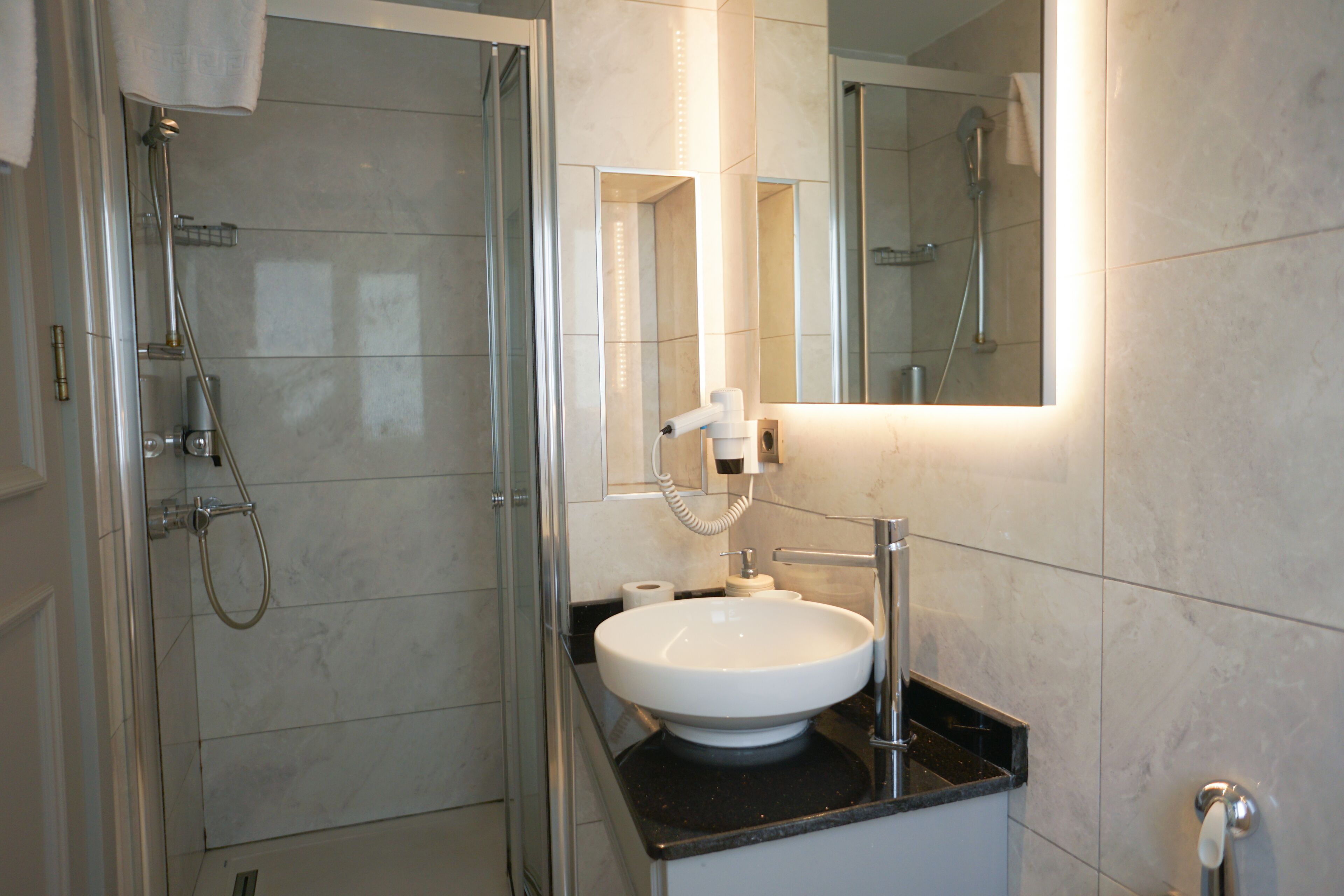 A modern bathroom with a glass-enclosed shower, a white sink, and a mirror with integrated lighting.