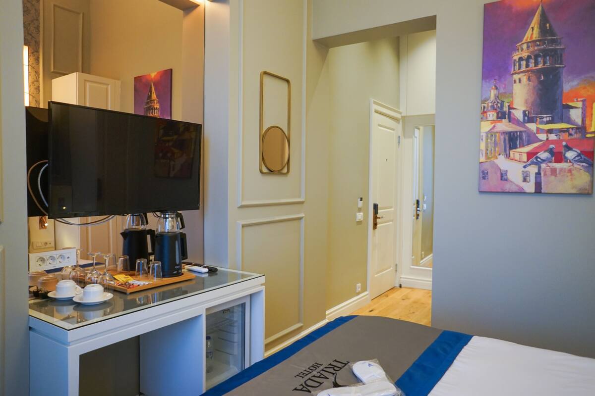 A hotel room with a bed, a desk with a coffee maker, a television, and a painting on the wall.