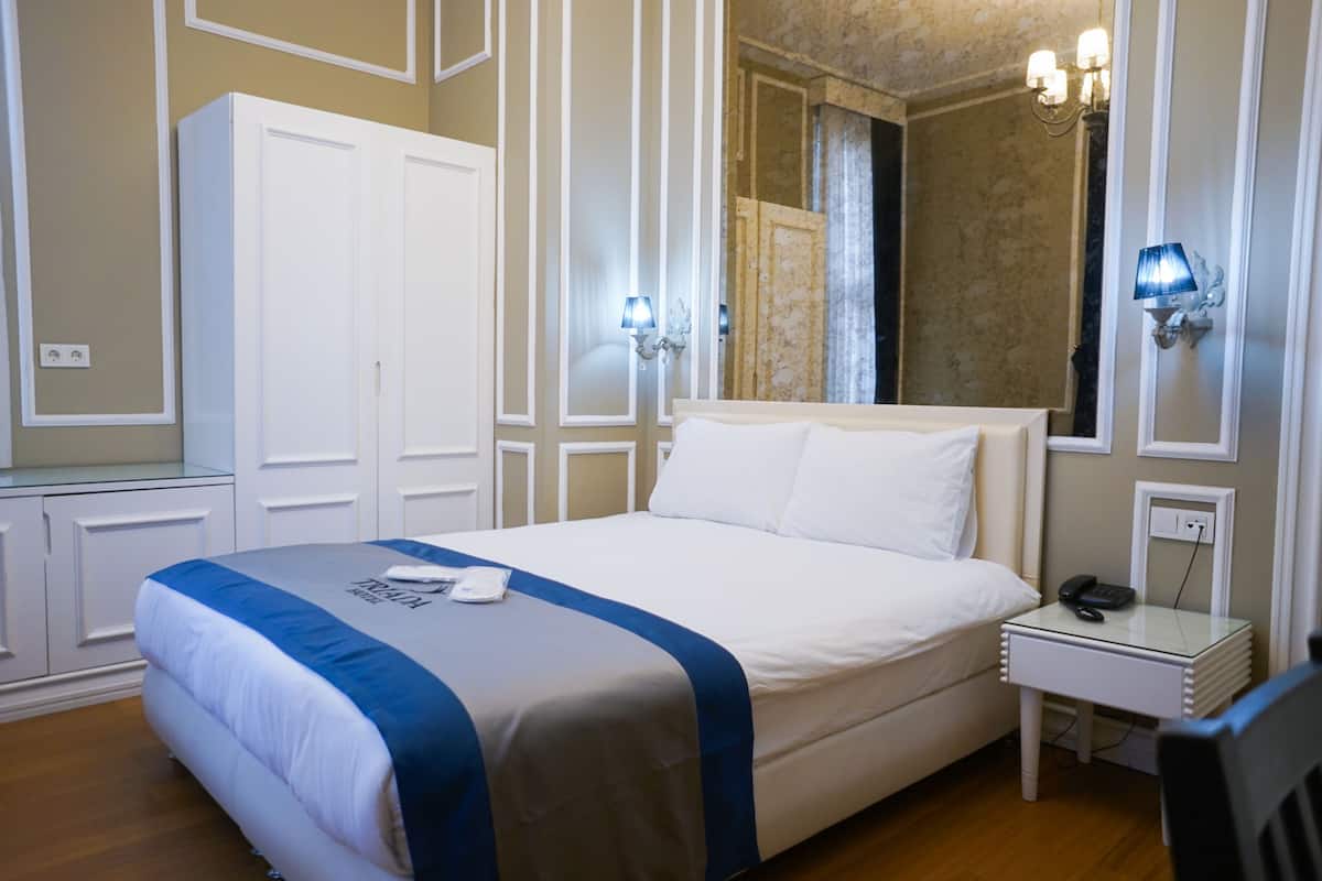 A hotel room with a bed, a wardrobe, a bedside table with a lamp, and a mirror.