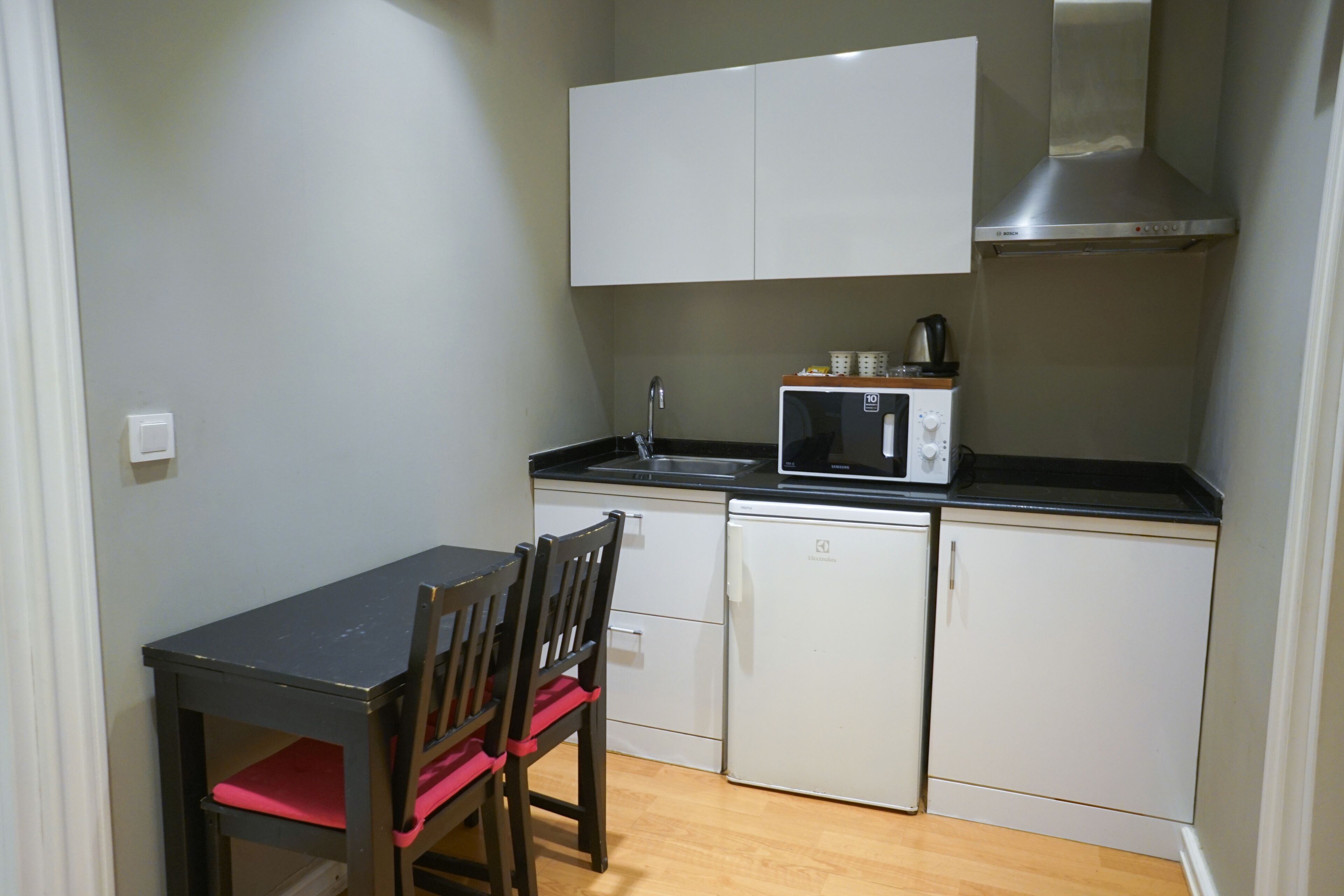 A compact kitchen with a microwave, sink, and cabinets. There is a small dining table with chairs.