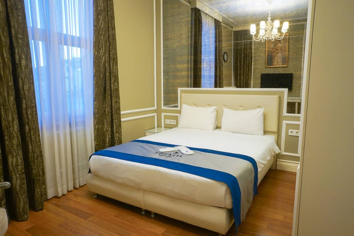 A neatly made bed with a blue and white bedspread, a bedside table, and a chandelier.