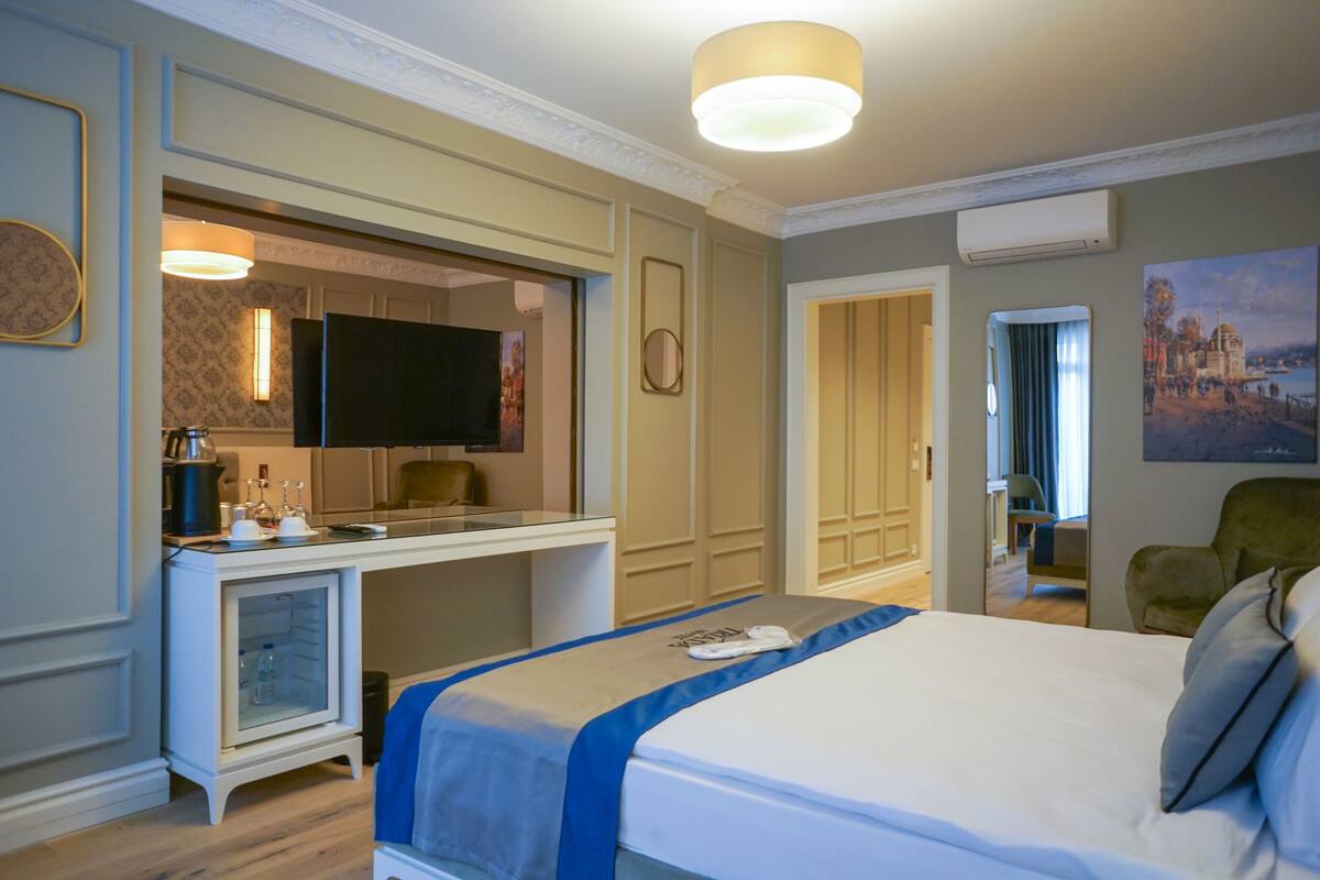 A hotel room with a bed, a desk, a television, and a painting on the wall.
