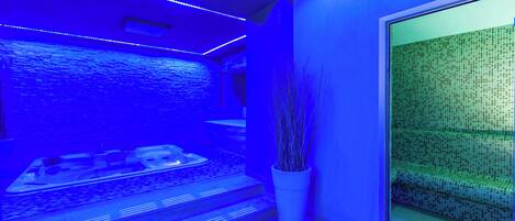 A modern spa room with a water feature, a seating area, and a potted plant.