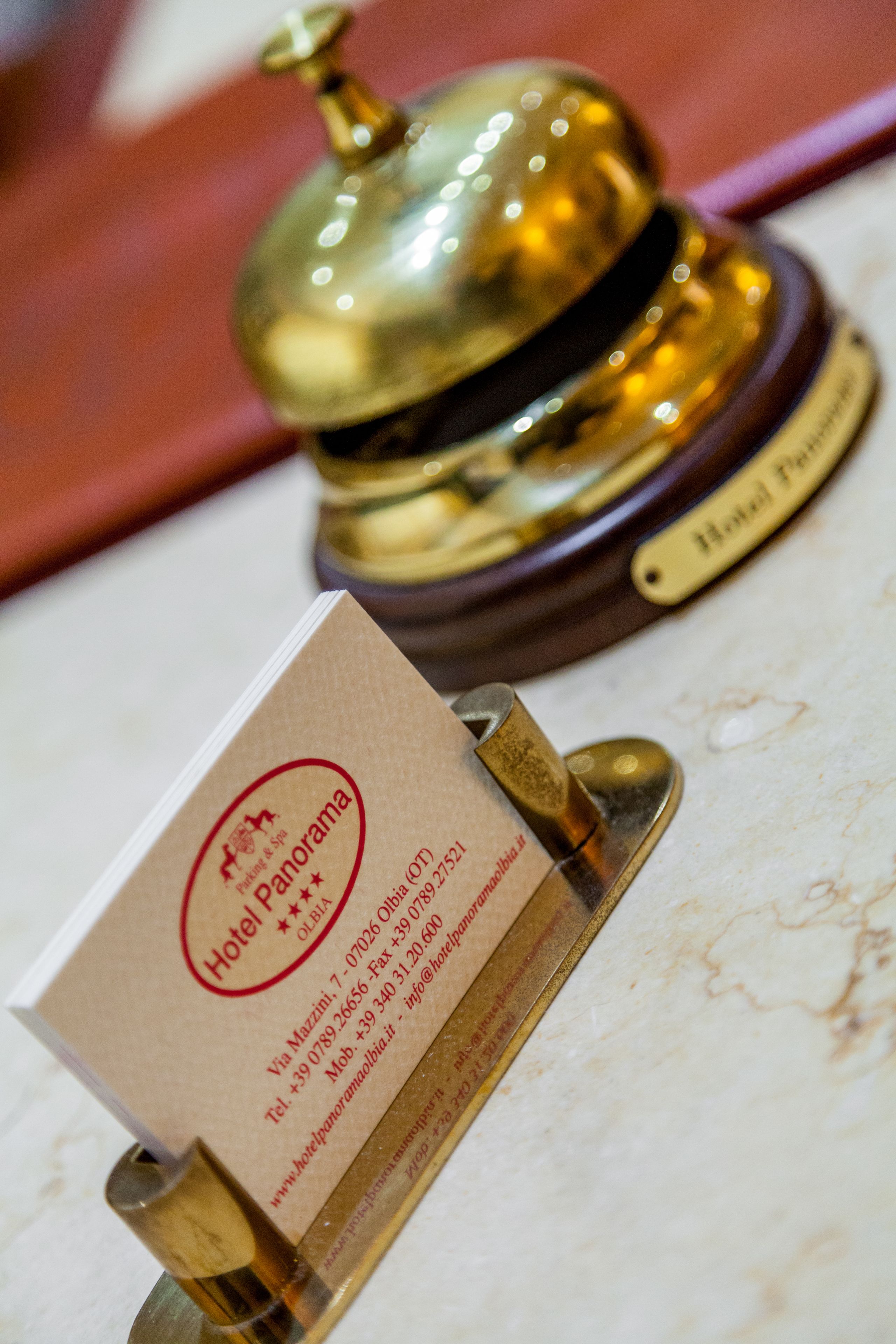 A hotel reception desk with a brass bell and a business card.