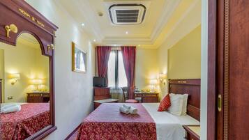 A hotel room with a large bed, a smaller bed, a desk, a chair, a TV, and a mirror.
