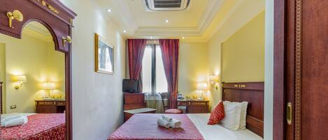 A hotel room with a large bed, a smaller bed, a desk, a chair, a TV, and a mirror.