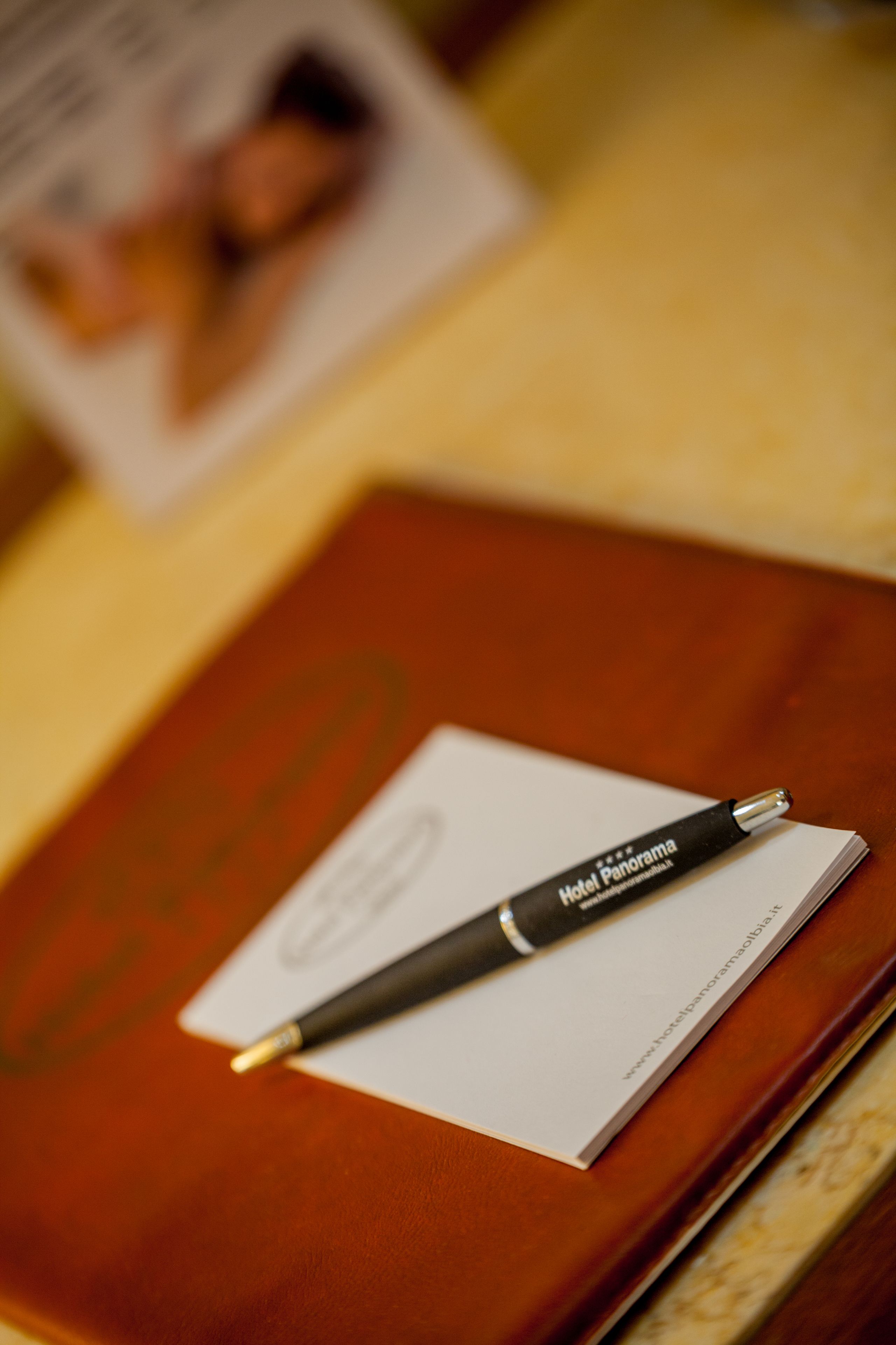 A notebook with a pen on top, a business card, and a blurred background.