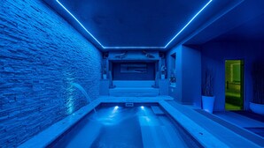 Un área de piscina interior moderna con una pared de piedra, un banco y una puerta que da al exterior.