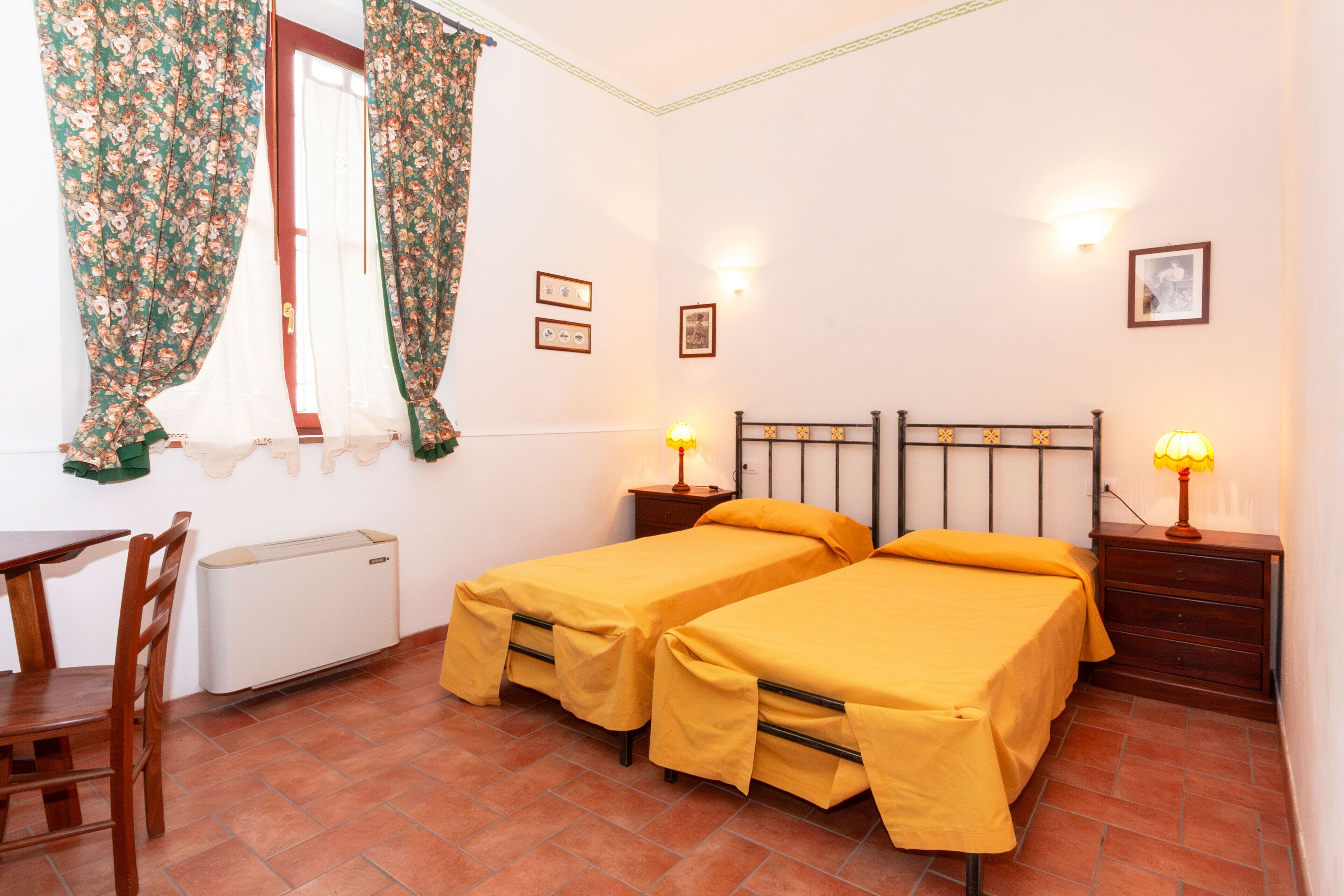 Une chambre avec deux lits simples, un bureau, une chaise, un radiateur et deux lampes de chevet.
