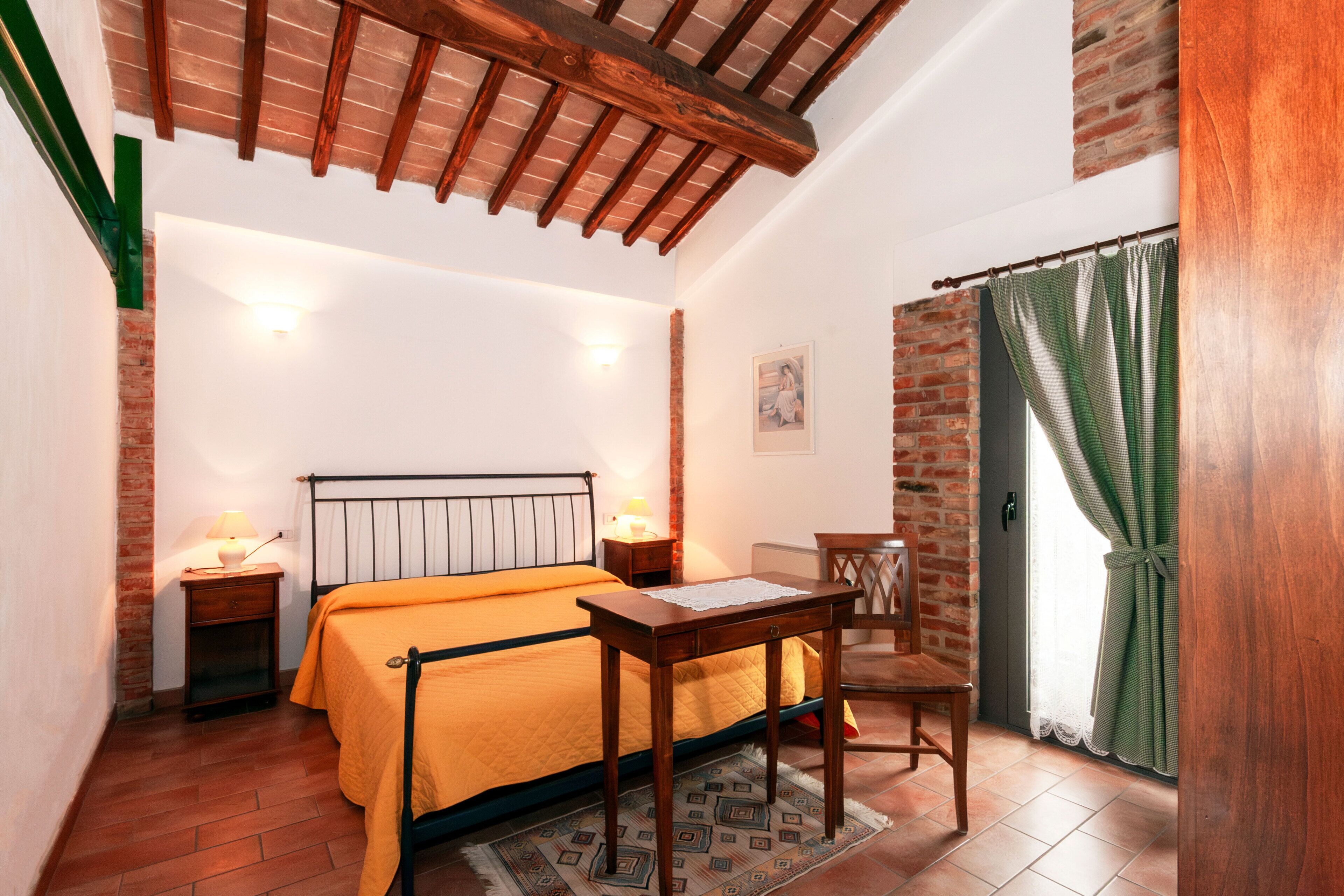 A bedroom with a bed, bedside tables, a chair, a table, and a window with curtains.