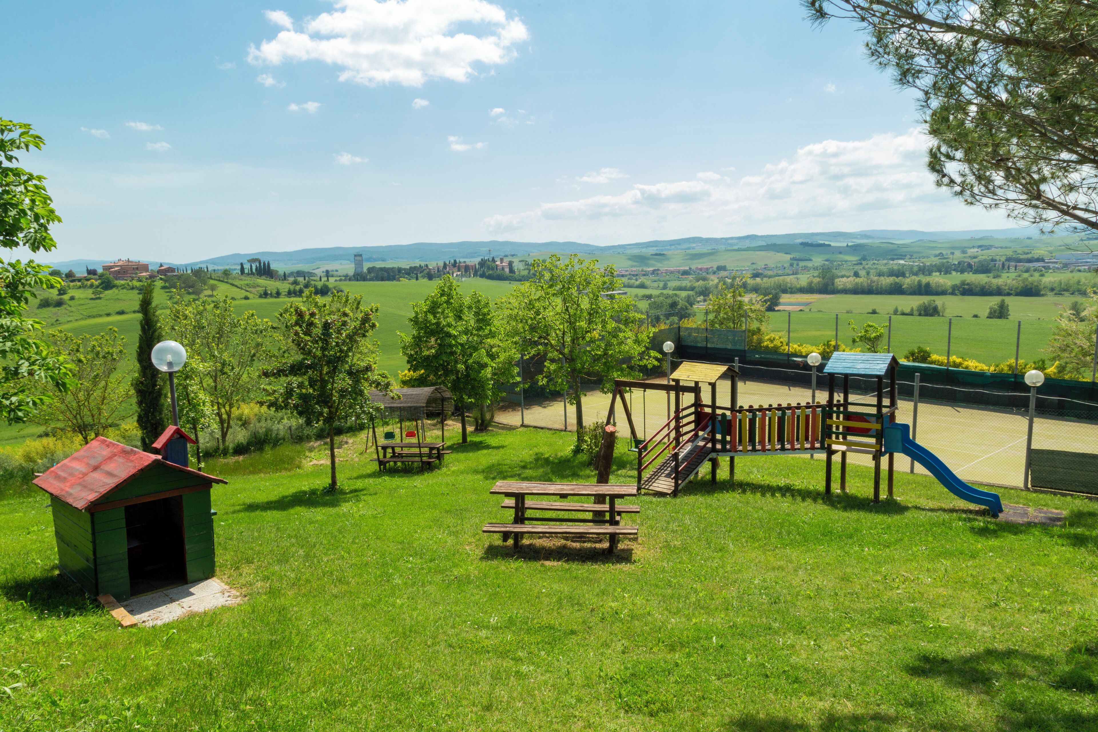A playground with a slide, swings, and a picnic table in a grassy area with a view of distant hills.