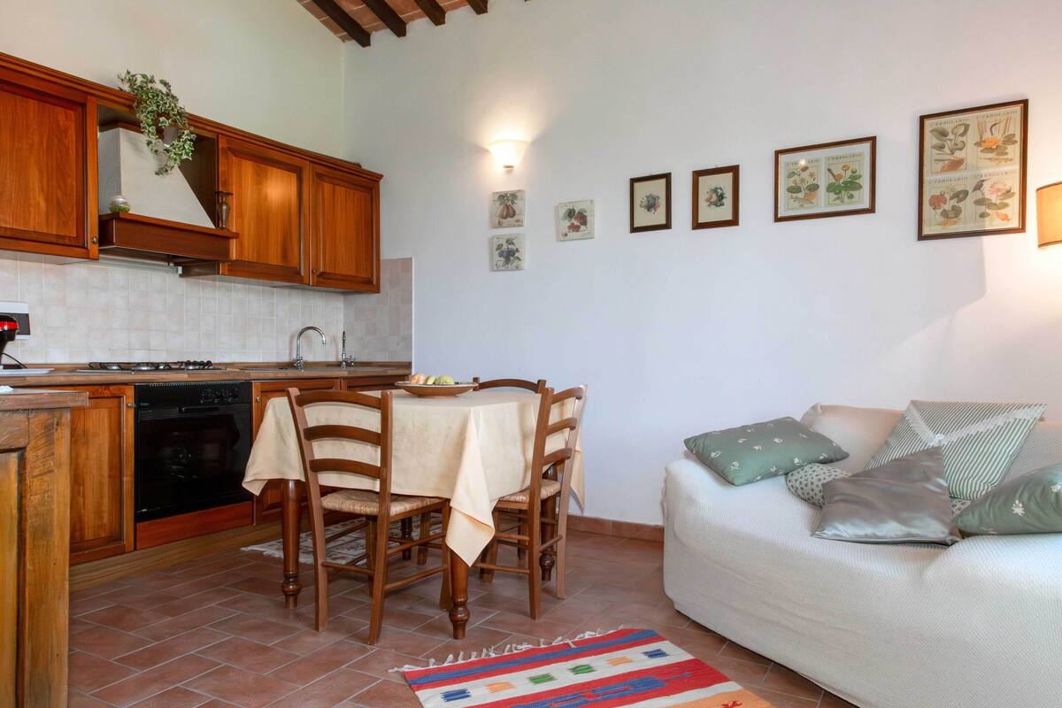 Una cocina compacta con armarios de madera, una mesa de comedor con sillas, un sofá con cojines y piso de baldosas.