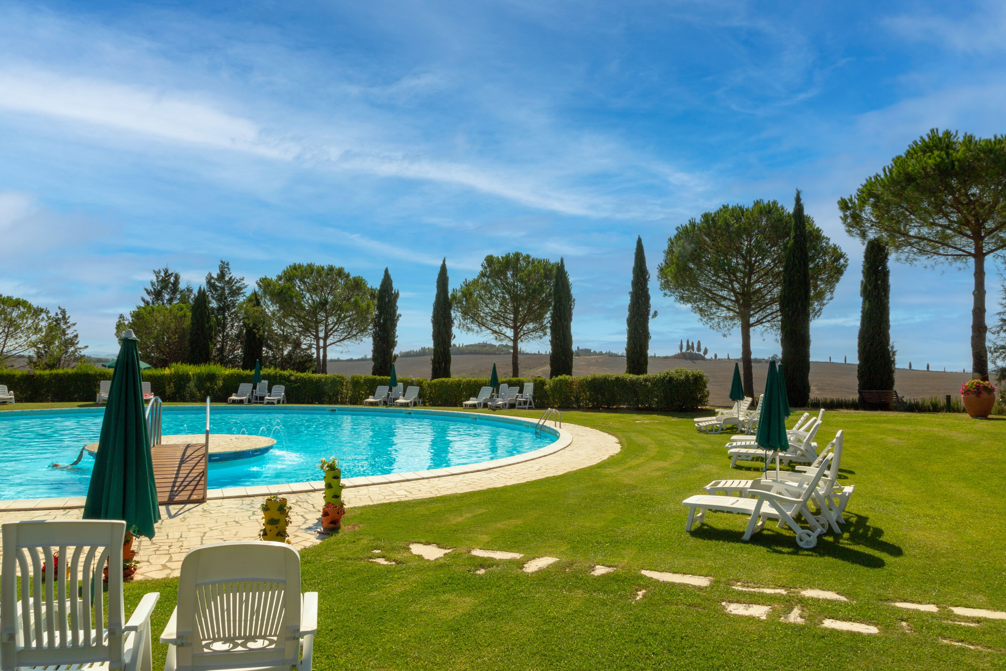 A swimming pool with lounge chairs and umbrellas, surrounded by well-maintained grass and trees.