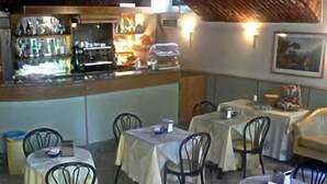 Un restaurant amb taules i cadires rodones, una zona de bar i un mural a la paret.