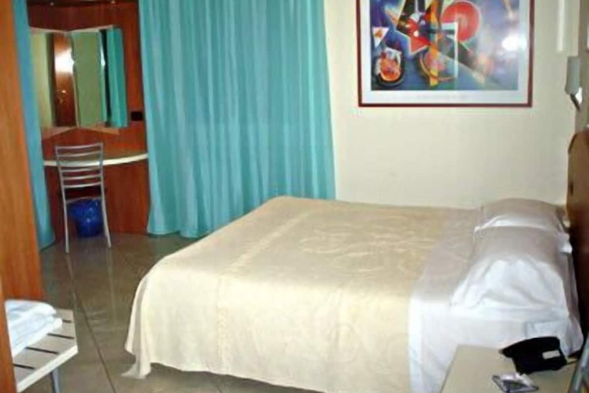 A hotel room with a bed, a desk, a chair, a television, and a painting on the wall.