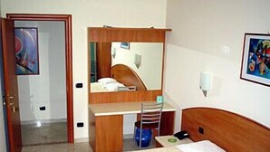 Una habitació d'hotel amb un llit, una taula de treball, una cadira, un mirall i una porta.