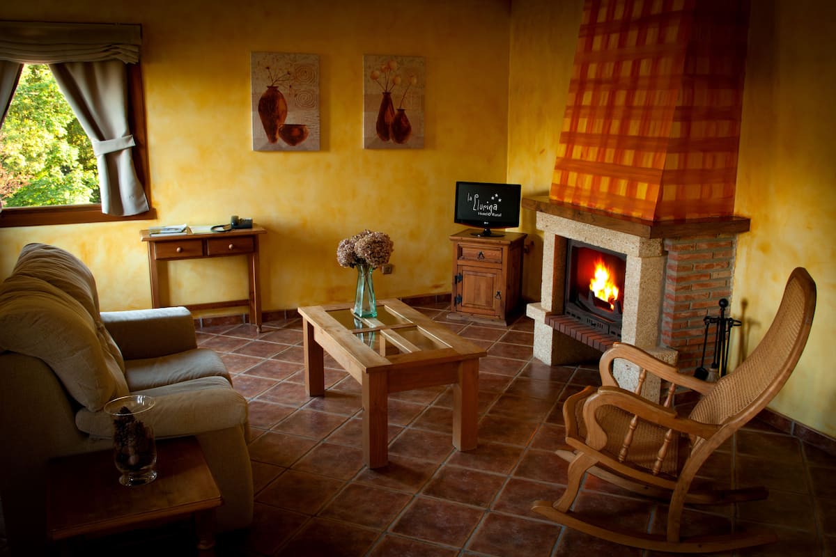 Una sala de estar acogedora con un sofá, una mesa de centro de madera, un sillón mecededor, una chimenea con detalles de ladrillo y un televisor sobre un mueble de madera.