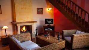 A cozy living room with wicker furniture, a fireplace, a television, and a staircase. - La Lluriga (Llanes)