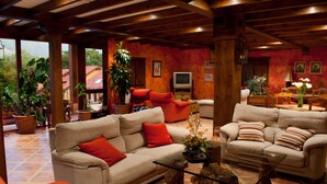 A spacious living area with two sofas, a coffee table, and a television. There are potted plants and a wooden ceiling. - La Lluriga (Llanes)