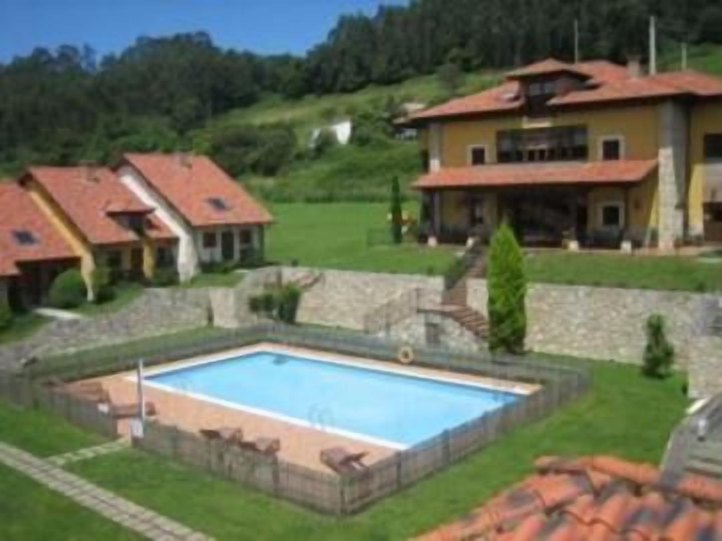 Zona residencial con piscina, casas de techo rojo y un muro de piedra.