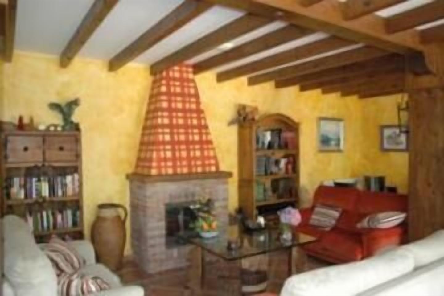 Una sala de estar acogedora con chimenea, vigas de madera, una estantería y un sofá rojo.