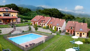 A residential area with a swimming pool surrounded by houses, a stone wall, and a mountain backdrop. - La Lluriga (Llanes)