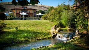 A house with a garden, a small stream, and outdoor seating. - La Lluriga (Llanes)