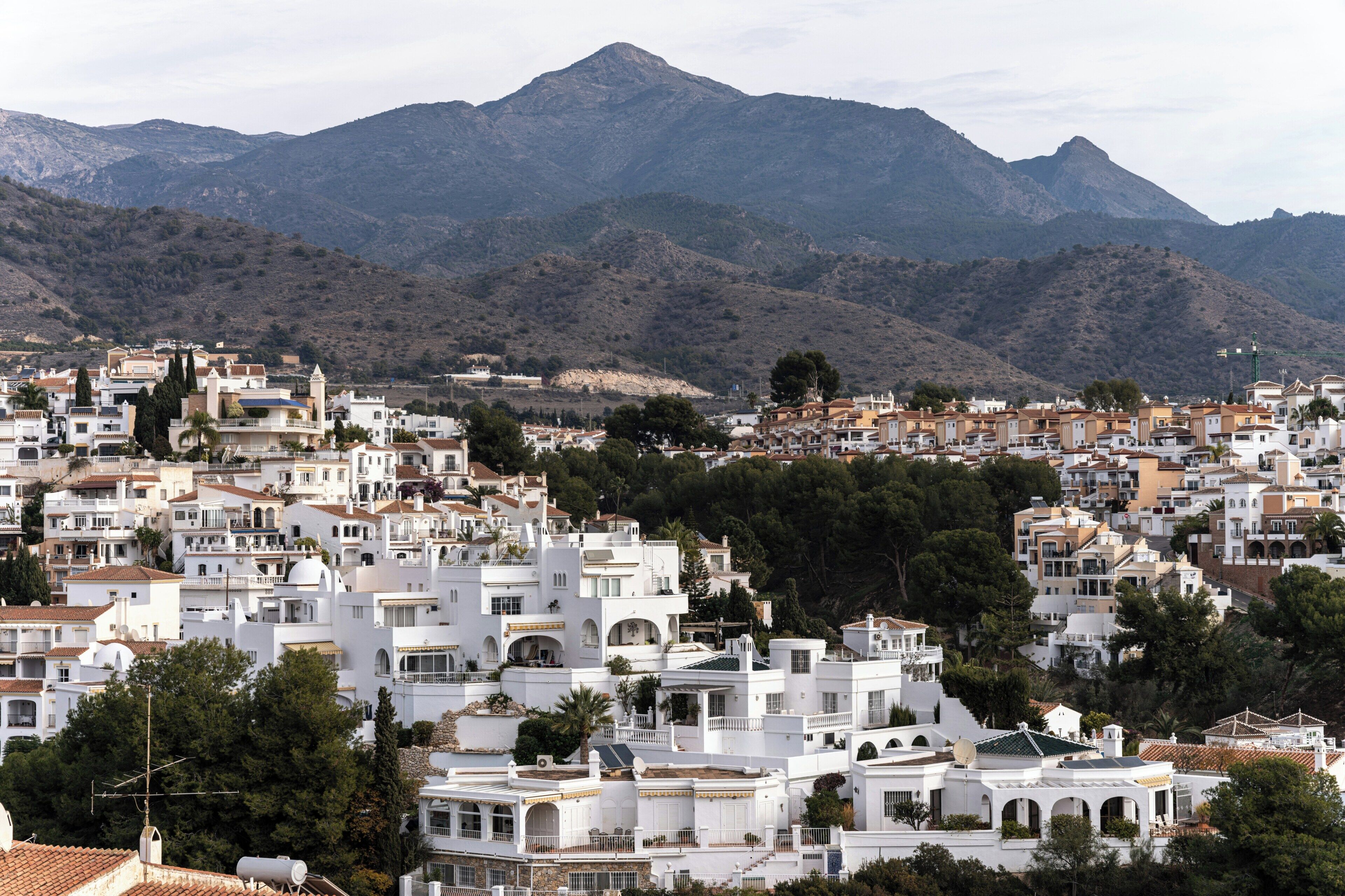 A densely packed town with white buildings, some with domed roofs, and a mountain range in the background.