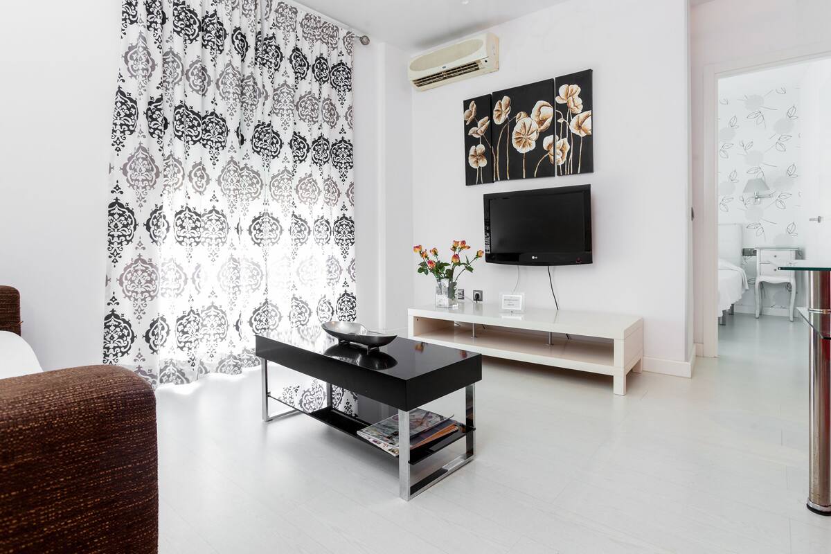 Una sala de estar moderna con una mesa de centro negra, un mueble blanco para el equipo de entretenimiento y un televisor de pantalla plana.