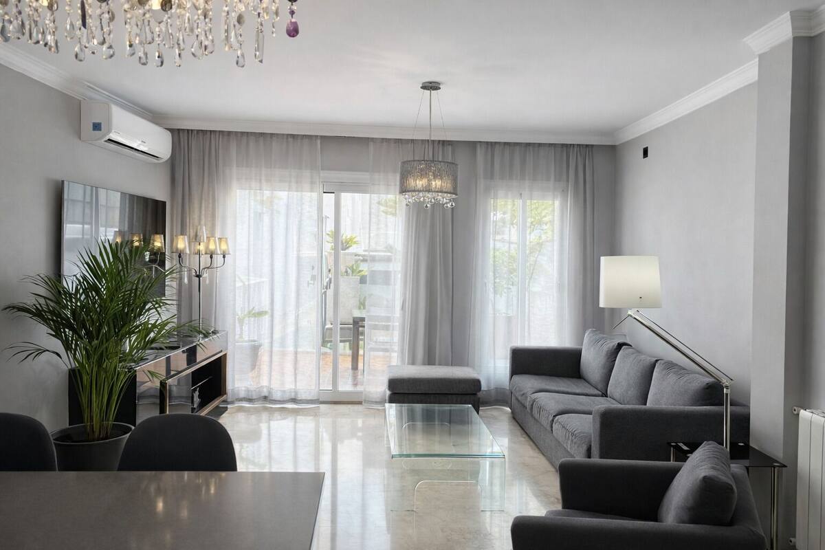 Una sala de estar moderna con un sofá, una mesa de centro de cristal, un televisor y una araña.