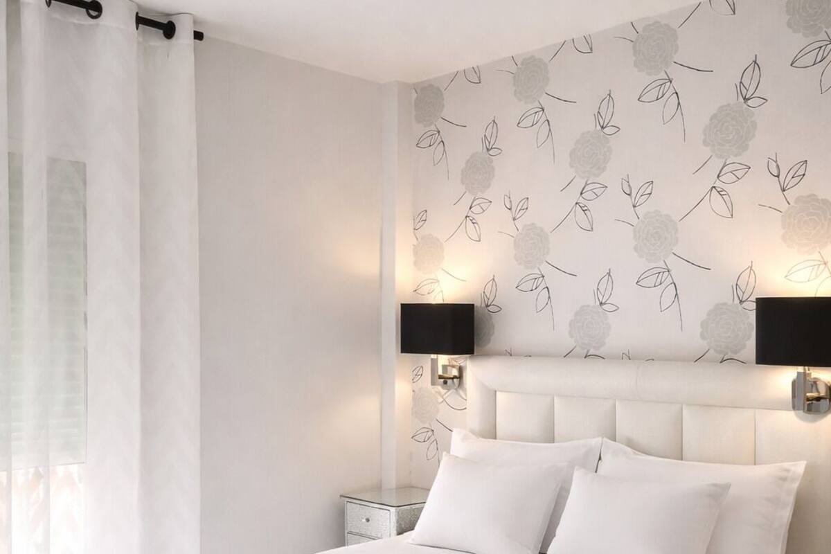 Un dormitorio moderno con una cama grande, ropa de cama blanca, un plaid negro y un papel tapiz con estampado floral.