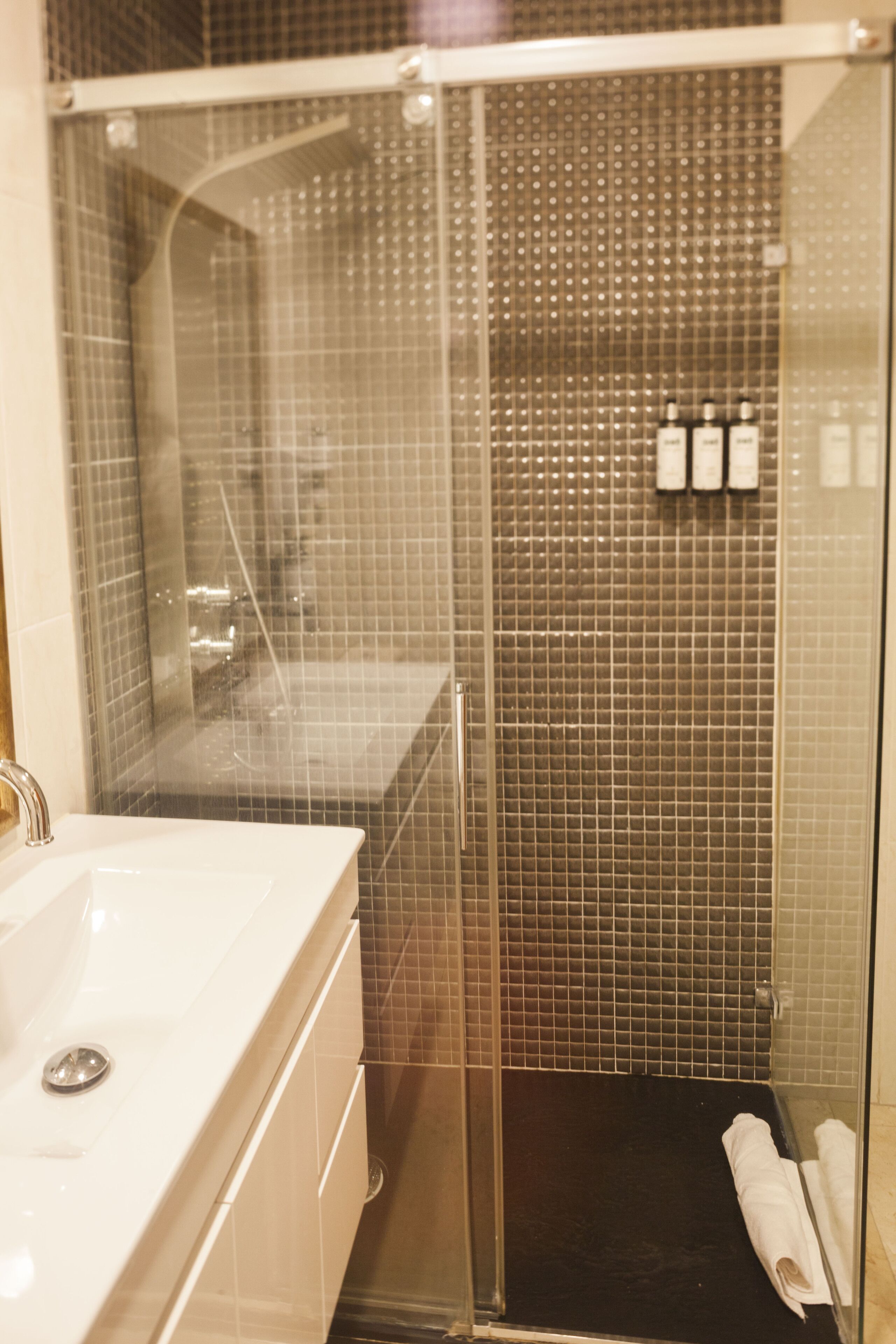 A modern bathroom with a glass-enclosed shower, a white sink, and a tiled wall.