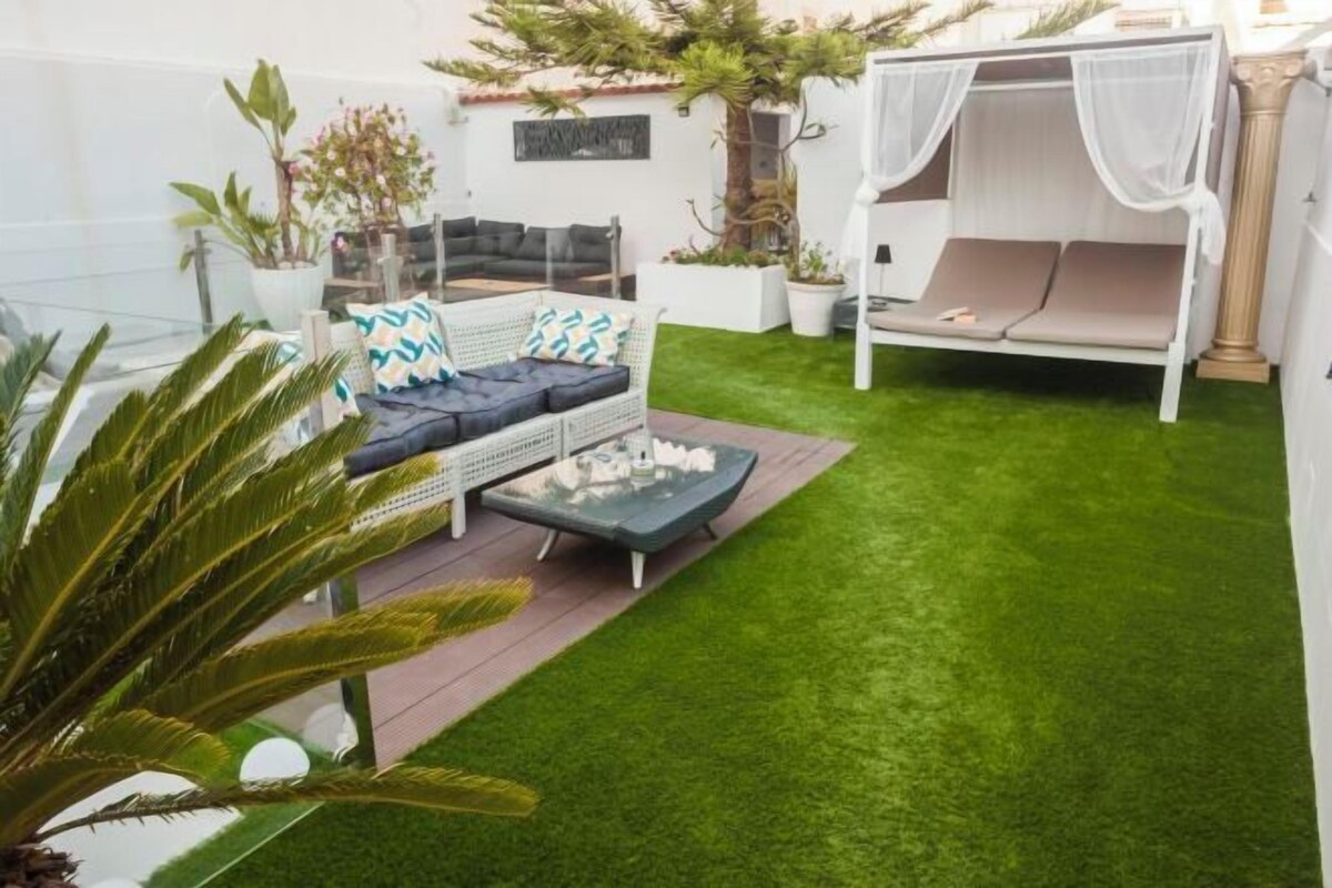 A patio area with a sofa, a small table, a white canopy bed, and artificial grass.