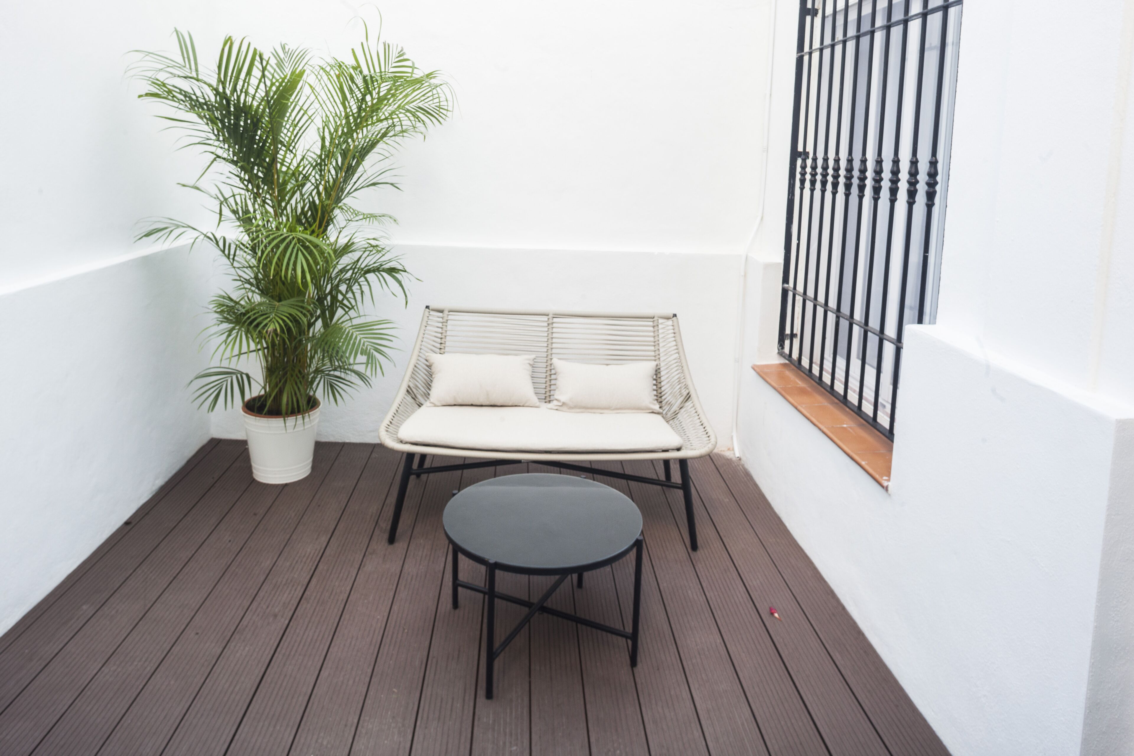 Ein Balkon mit einer Rattan-Couch, einem kleinen runden Tisch und einem Blumentopf.