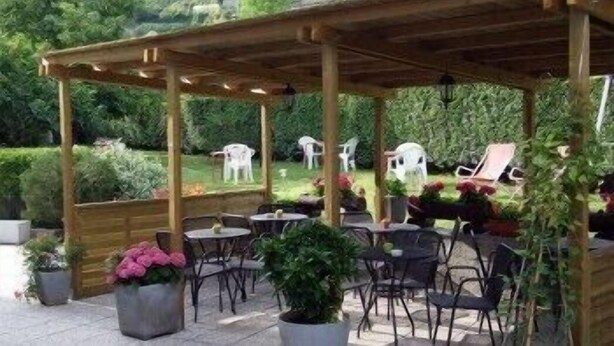 An outdoor patio area with wooden pergola, tables, and chairs, surrounded by greenery and hills. - Saint Pierre (Saint-Pierre)