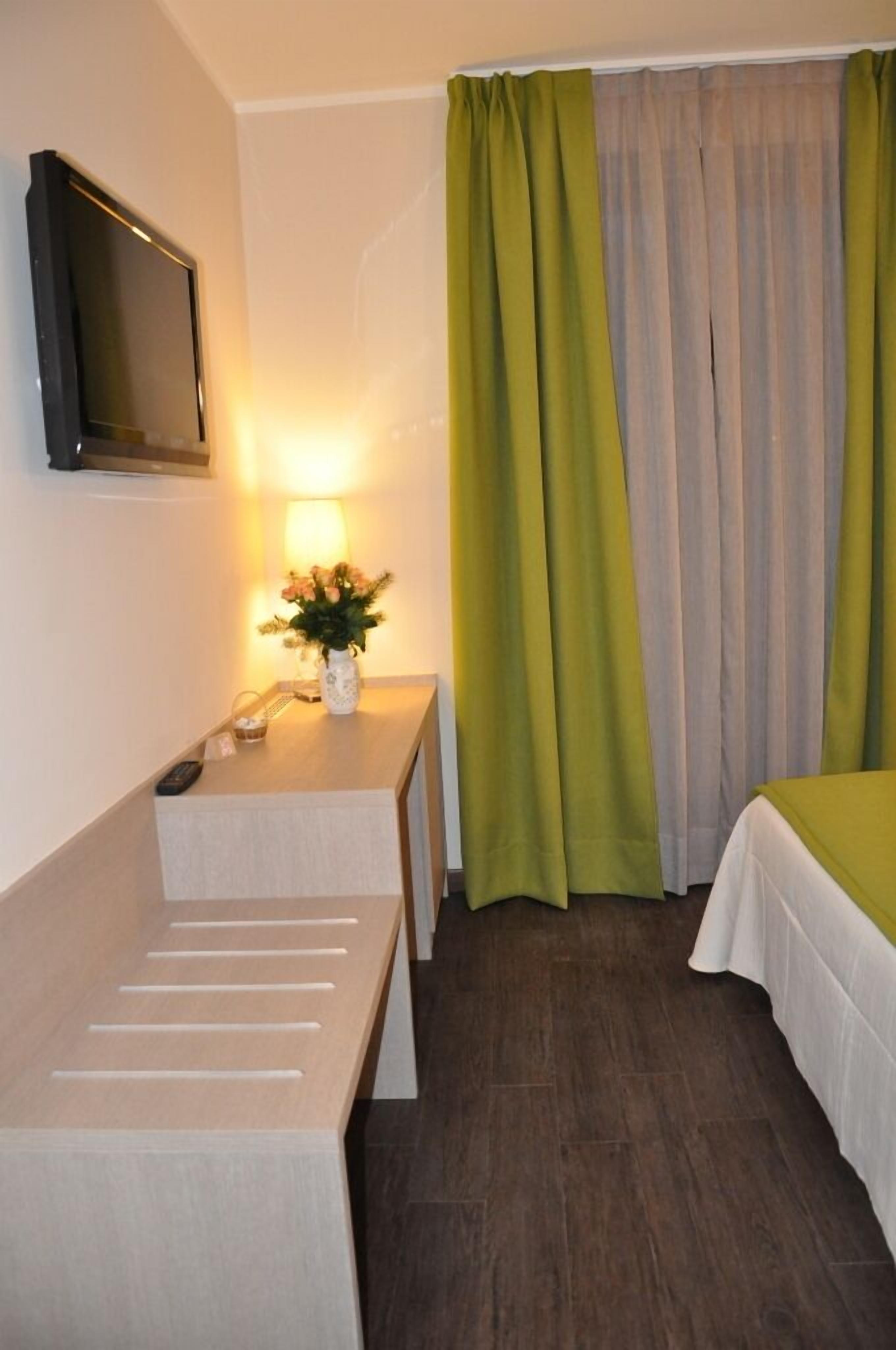 A hotel room with a bed, a bedside table with a lamp, a TV, and a window with curtains.