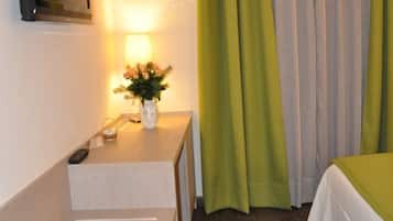 A hotel room with a bed, a bedside table with a lamp, a TV, and a window with curtains.
