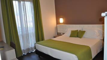 Una habitación de hotel con cama, cortinas verdes, una mesita de noche y una lámpara de pared.