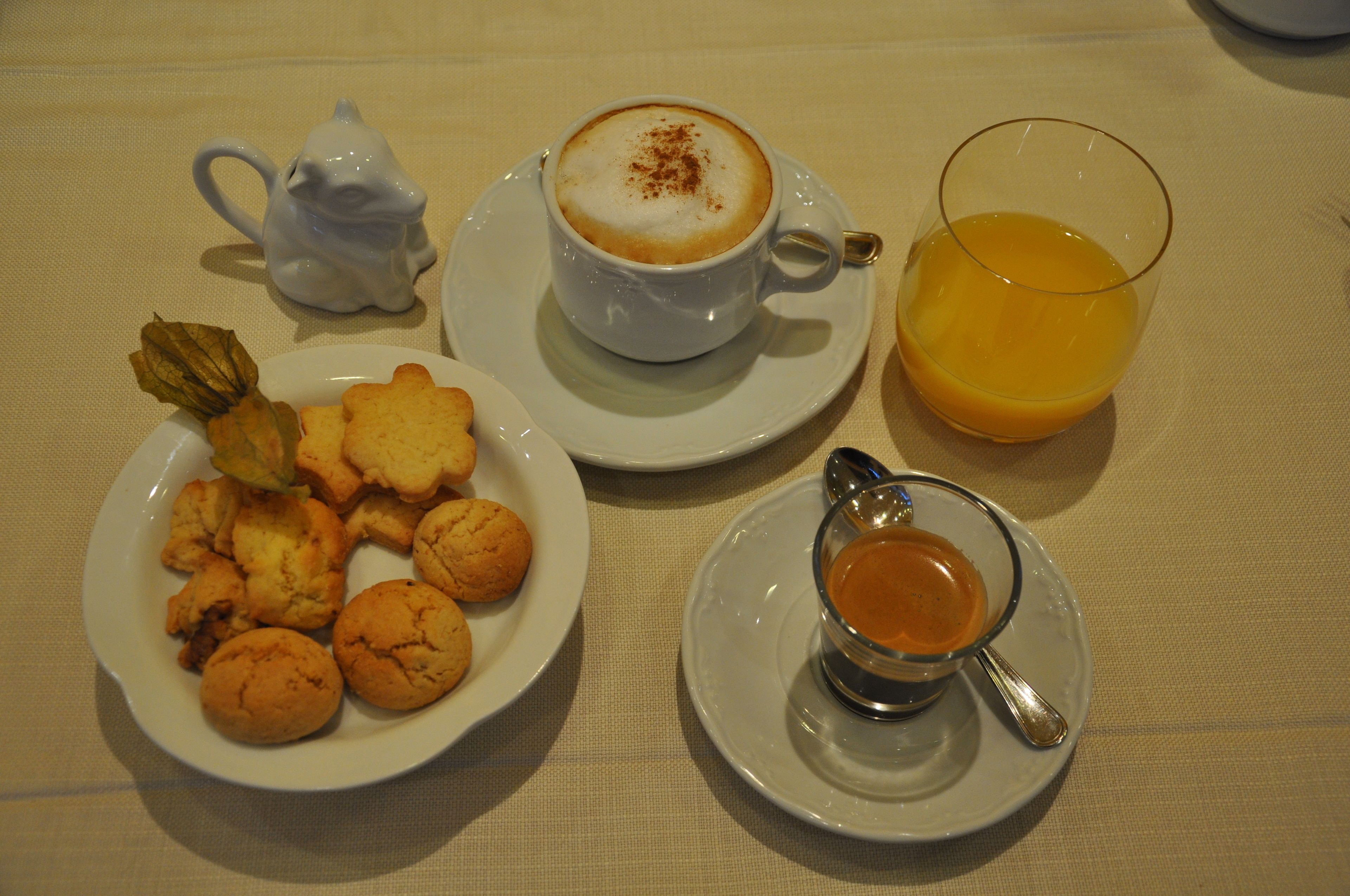 A breakfast setting with a cup of coffee, a glass of orange juice, a plate of cookies, and a small cup of tea.