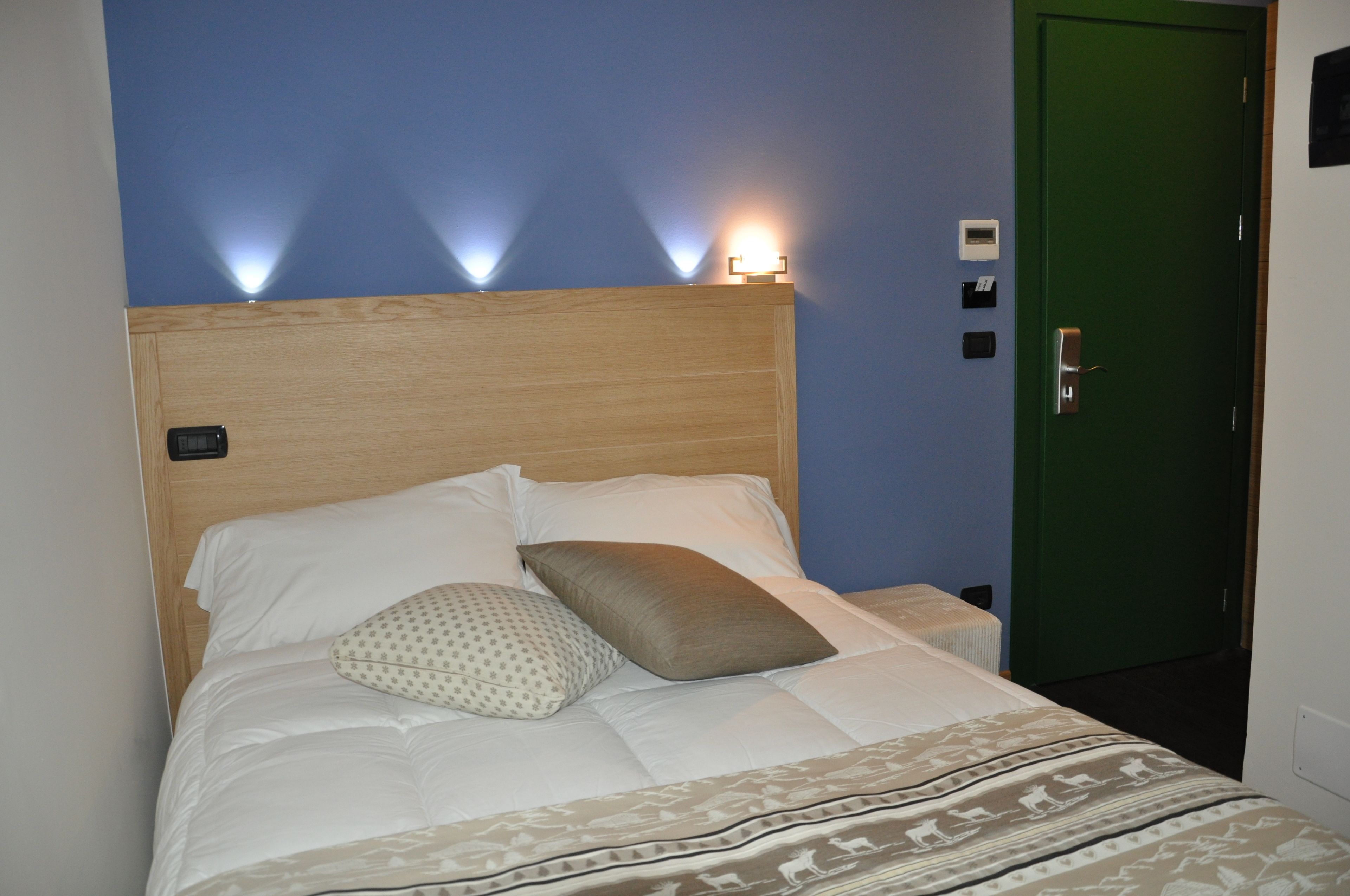 A neatly made bed with white and patterned pillows, a wooden headboard, and a green door to the right.
