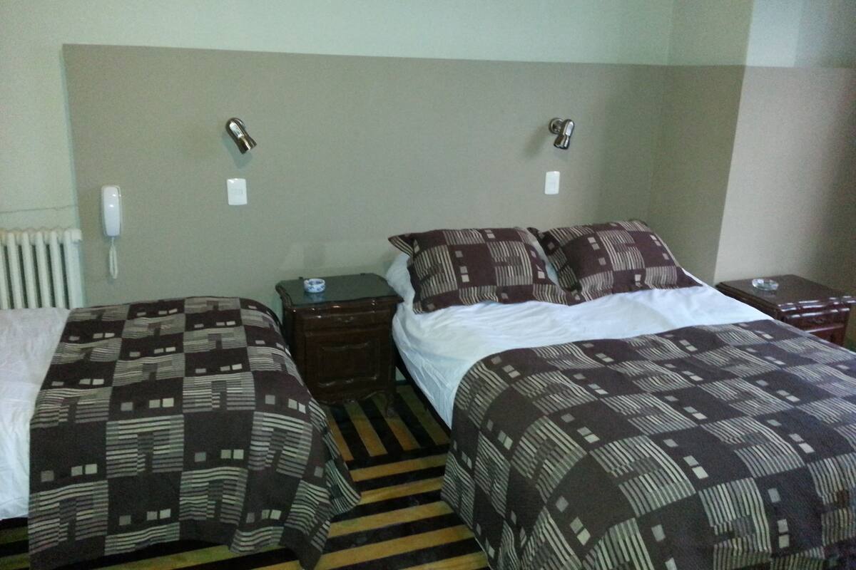 Habitación de hotel con dos camas individuales, una mesita de noche con lámpara, teléfono y radiador.
