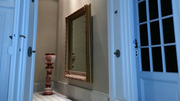 A hallway with a large mirror, a decorative vase, and a patterned floor. - New Arapey Hotel (Montevideo)